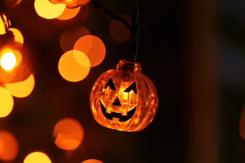 Glowing jack-o-lantern string light hanging in darkness with bokeh lights in background