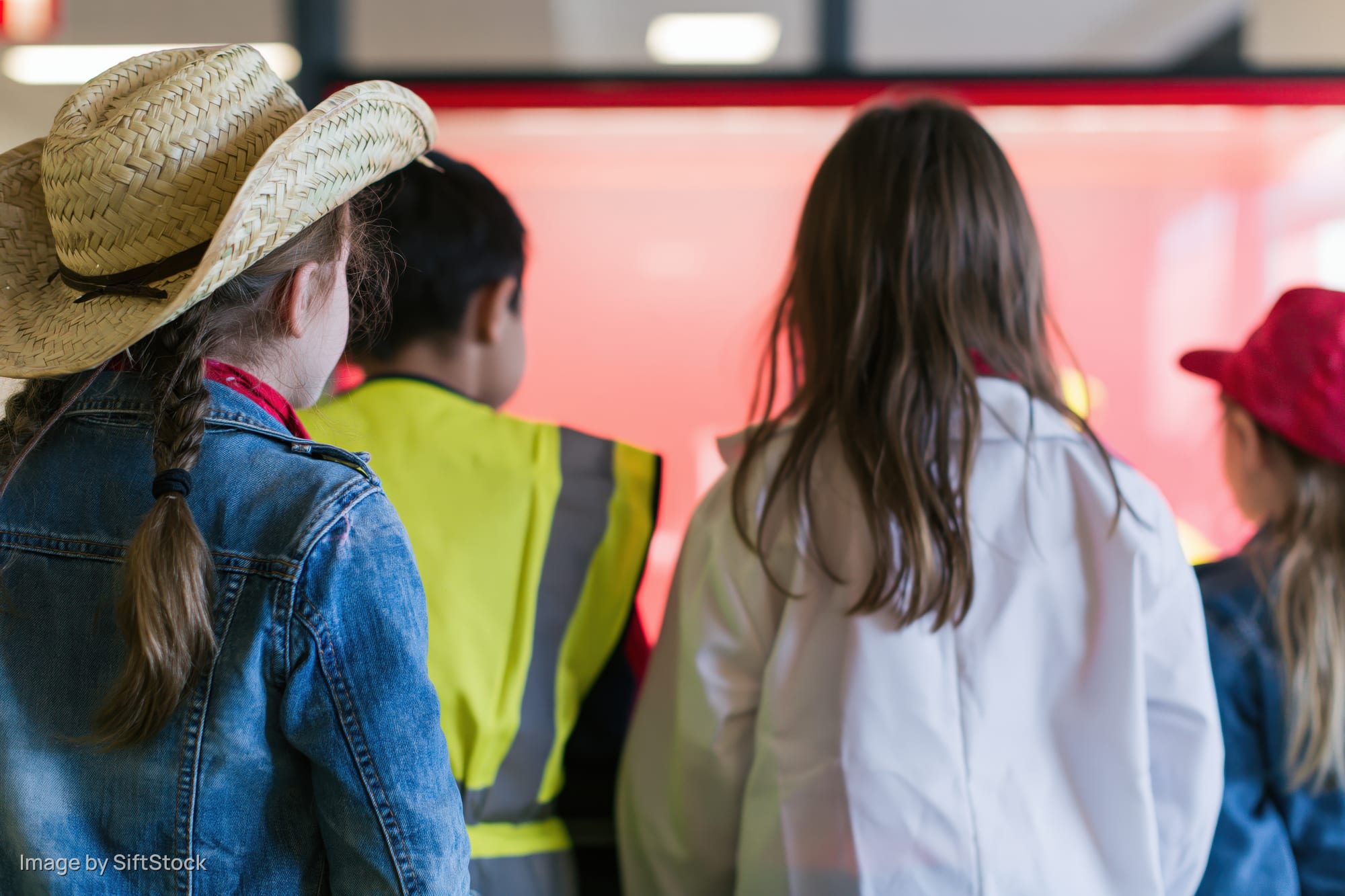 Children in costumes viewed from behind watching a glowing display in an indoor exhibit