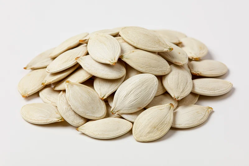 A heap of raw white pumpkin seeds on a plain white surface