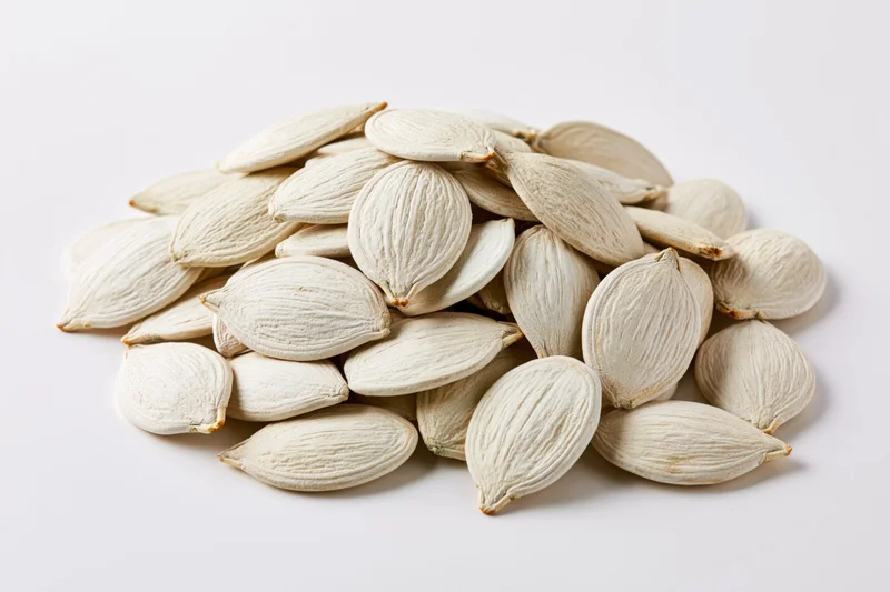 A heap of raw white pumpkin seeds on a plain white surface