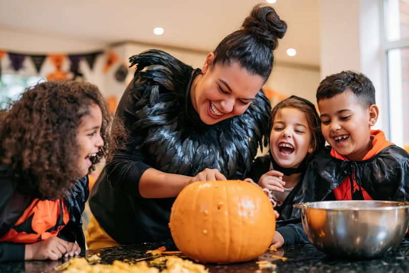 Woman carving a pumpkin with children in a kitchen during halloween celebration