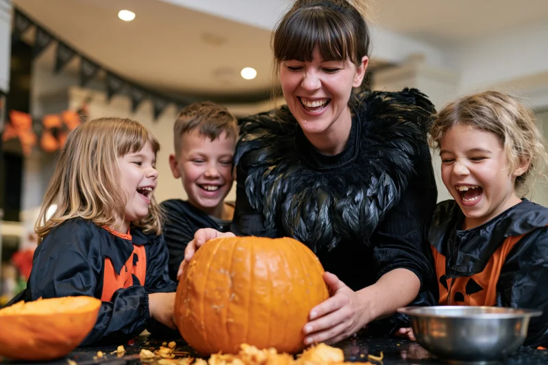 Woman and children laughing while carving a pumpkin at home for halloween