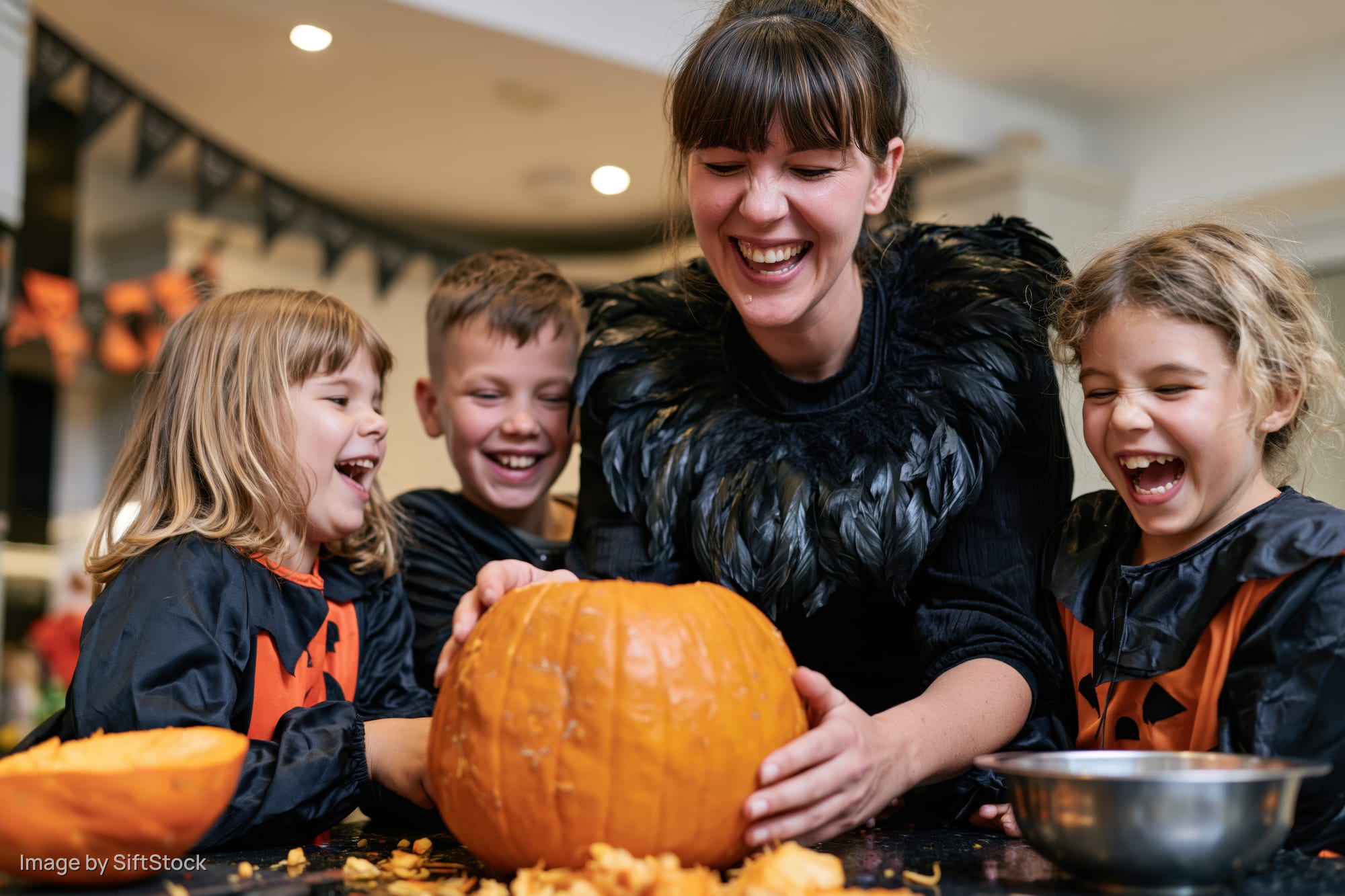 Woman and children laughing while carving a pumpkin at home for halloween