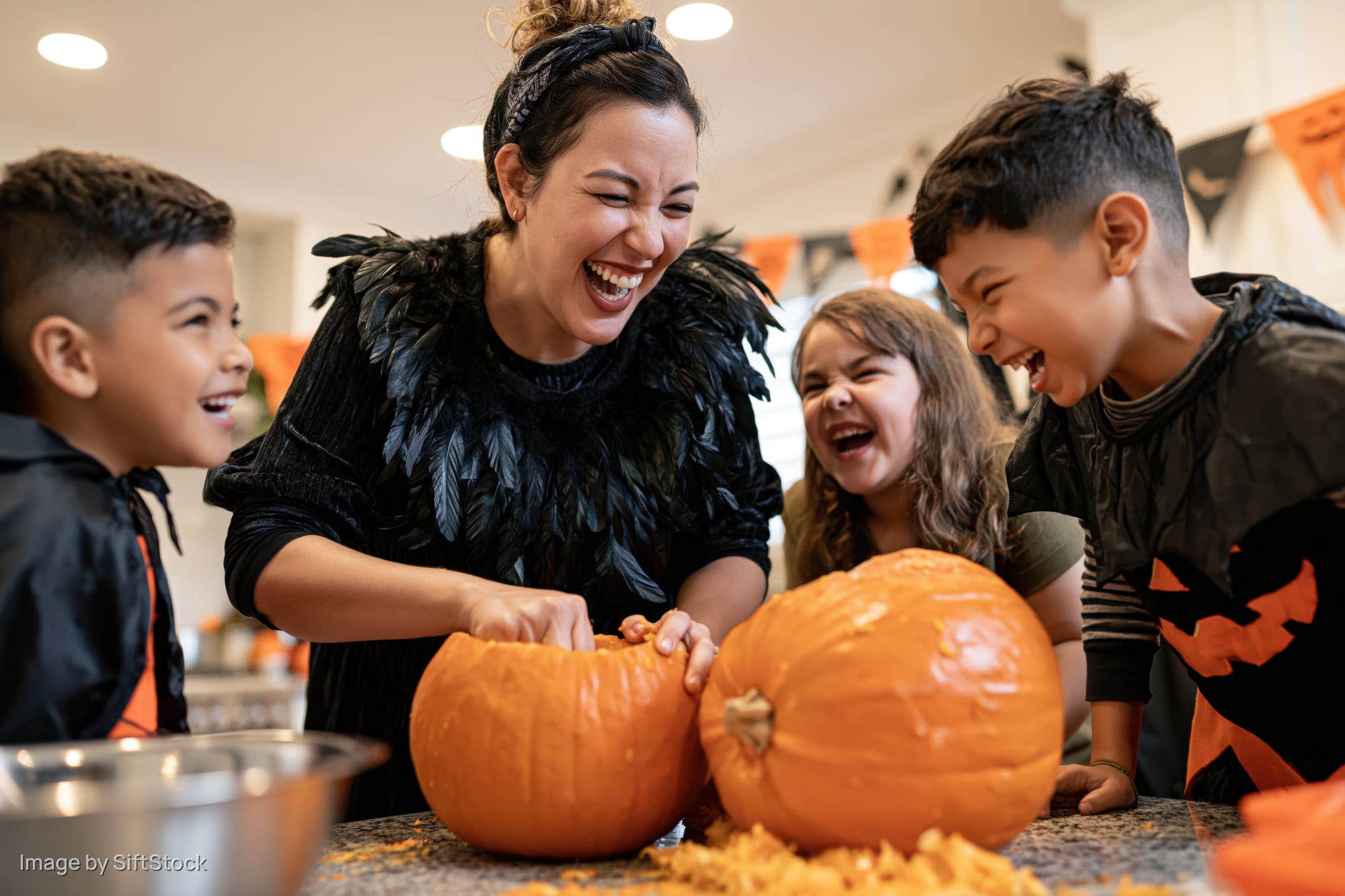 Woman carving pumpkin with children in kitchen during halloween celebration