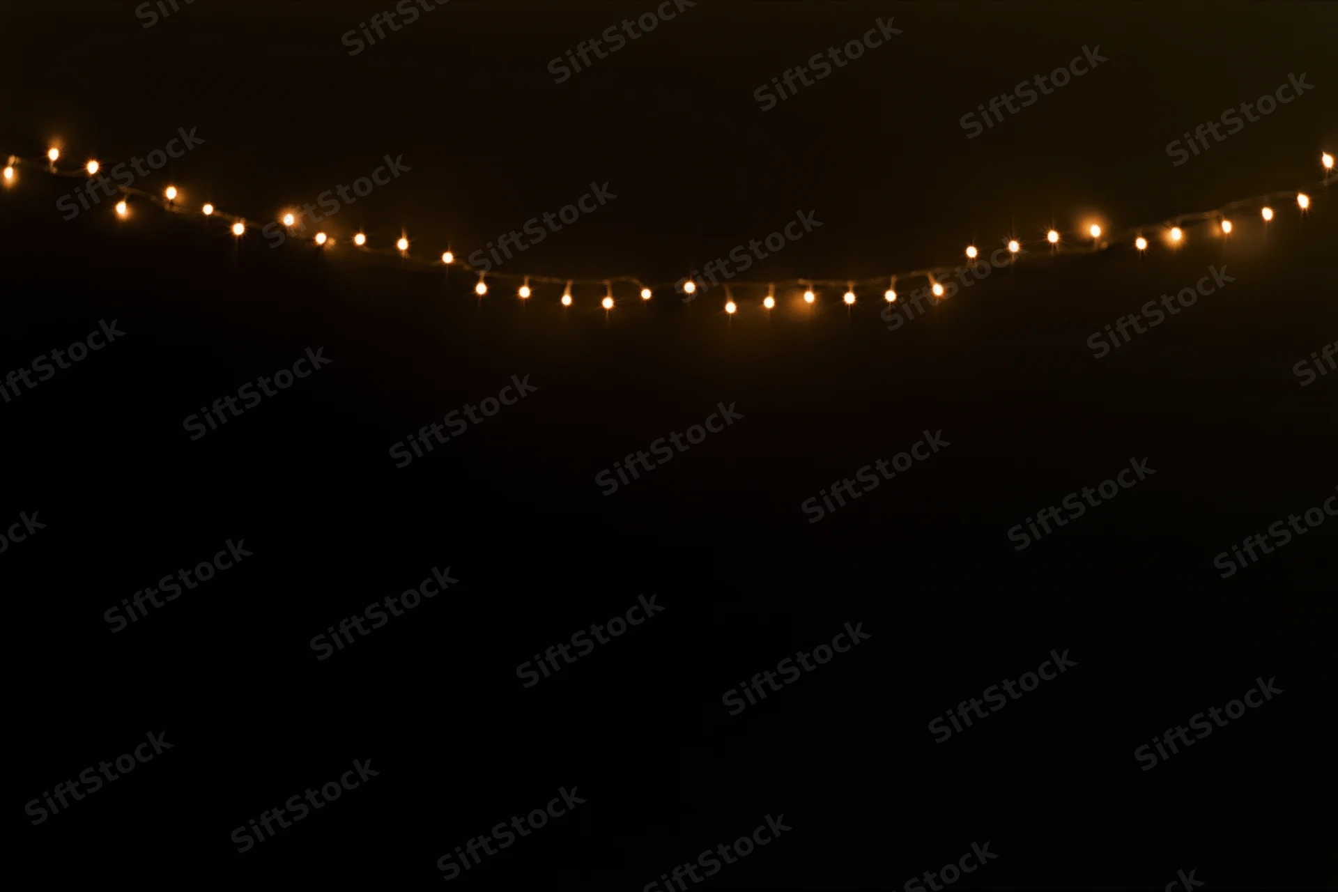 String of warm white fairy lights glowing against dark background with copyspace below