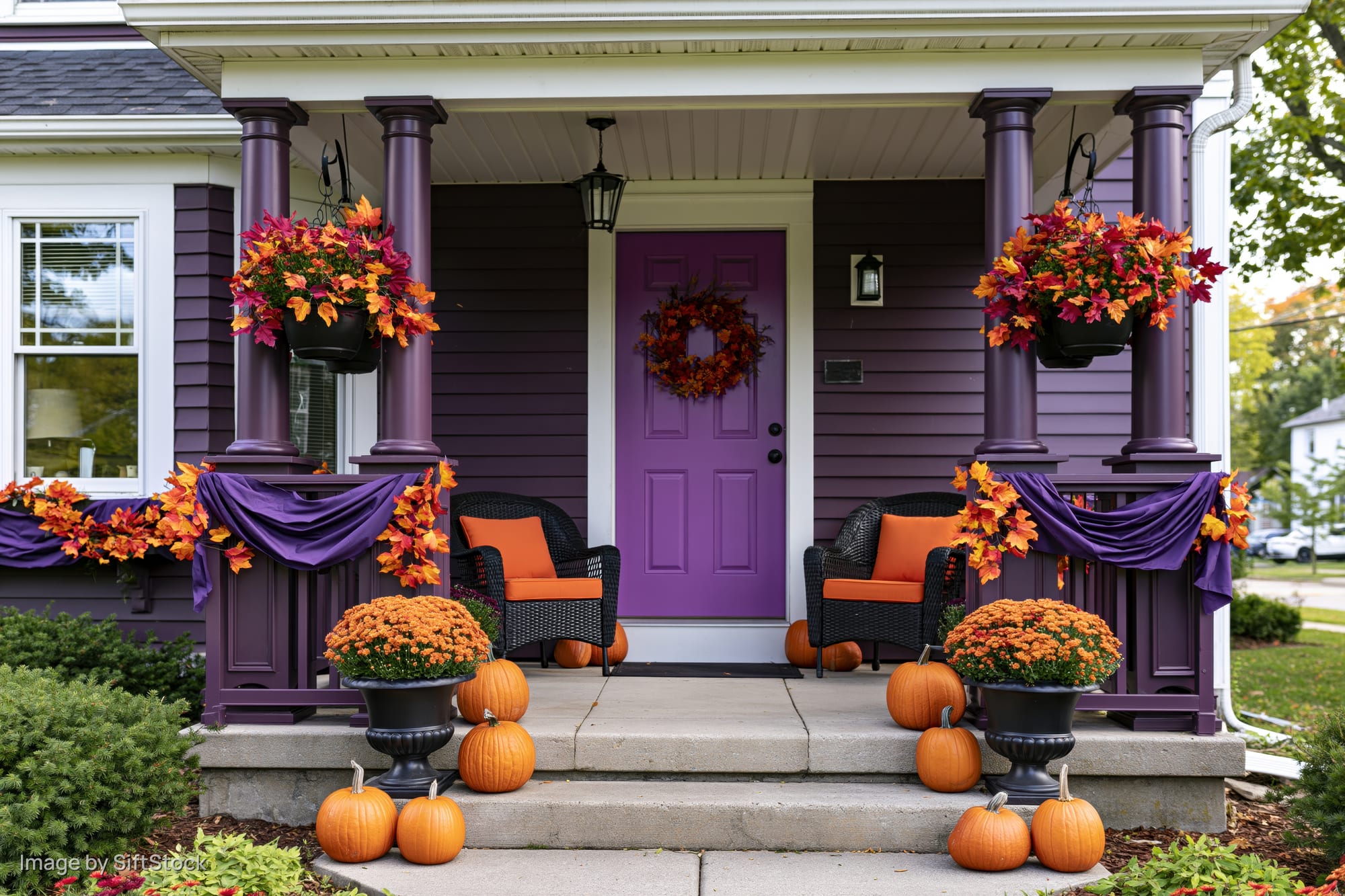 Purple front porch decorated with pumpkins, wreath, and autumn foliage for halloween
