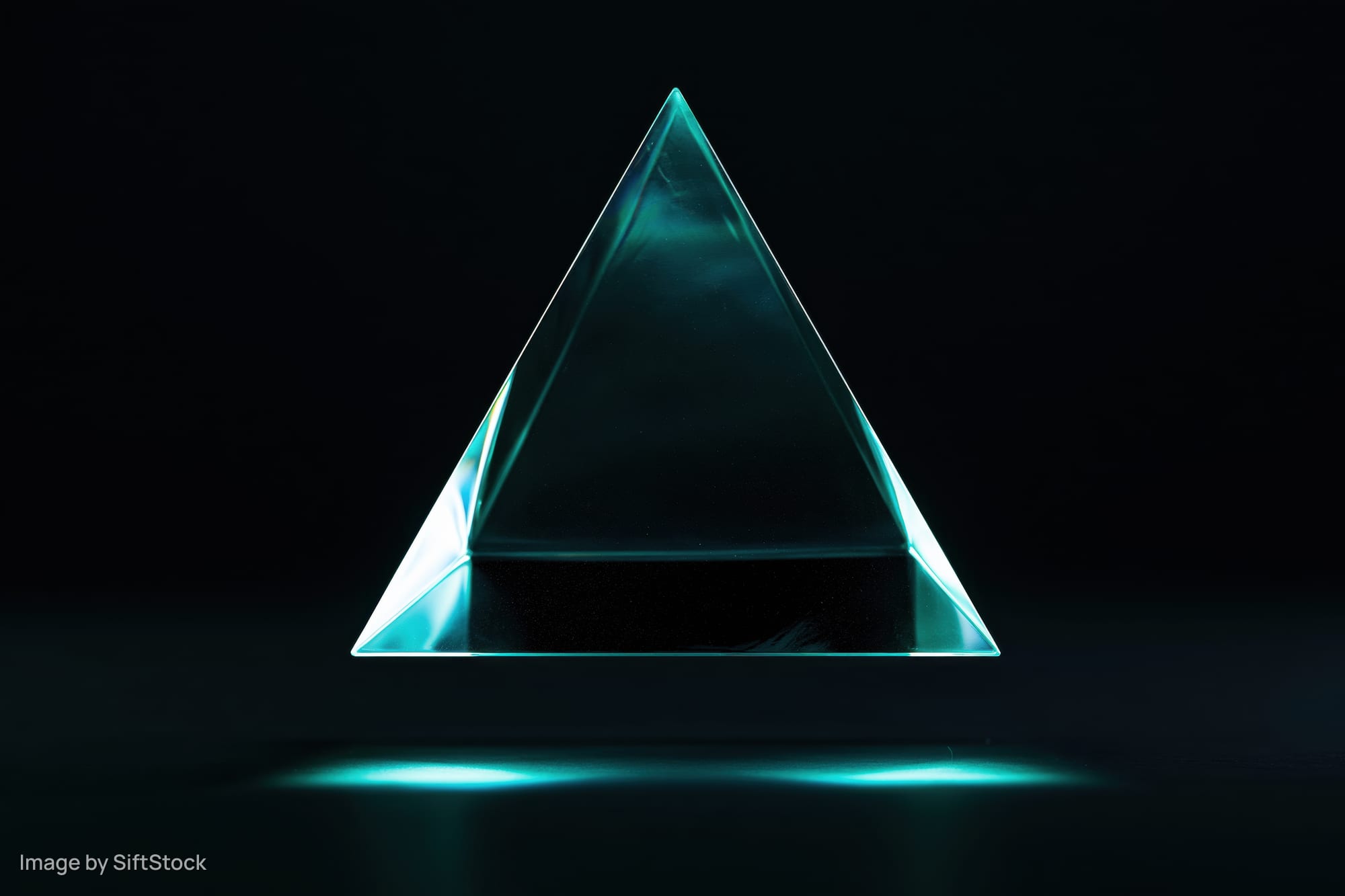 Translucent glass tetrahedron floating above dark surface with teal glow