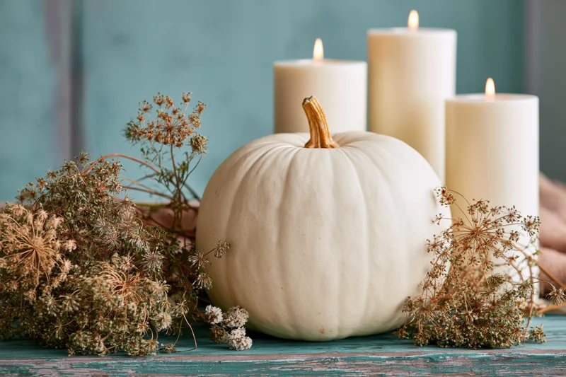 White heirloom pumpkin with lit candles and dried flowers arranged on a rustic teal wooden table