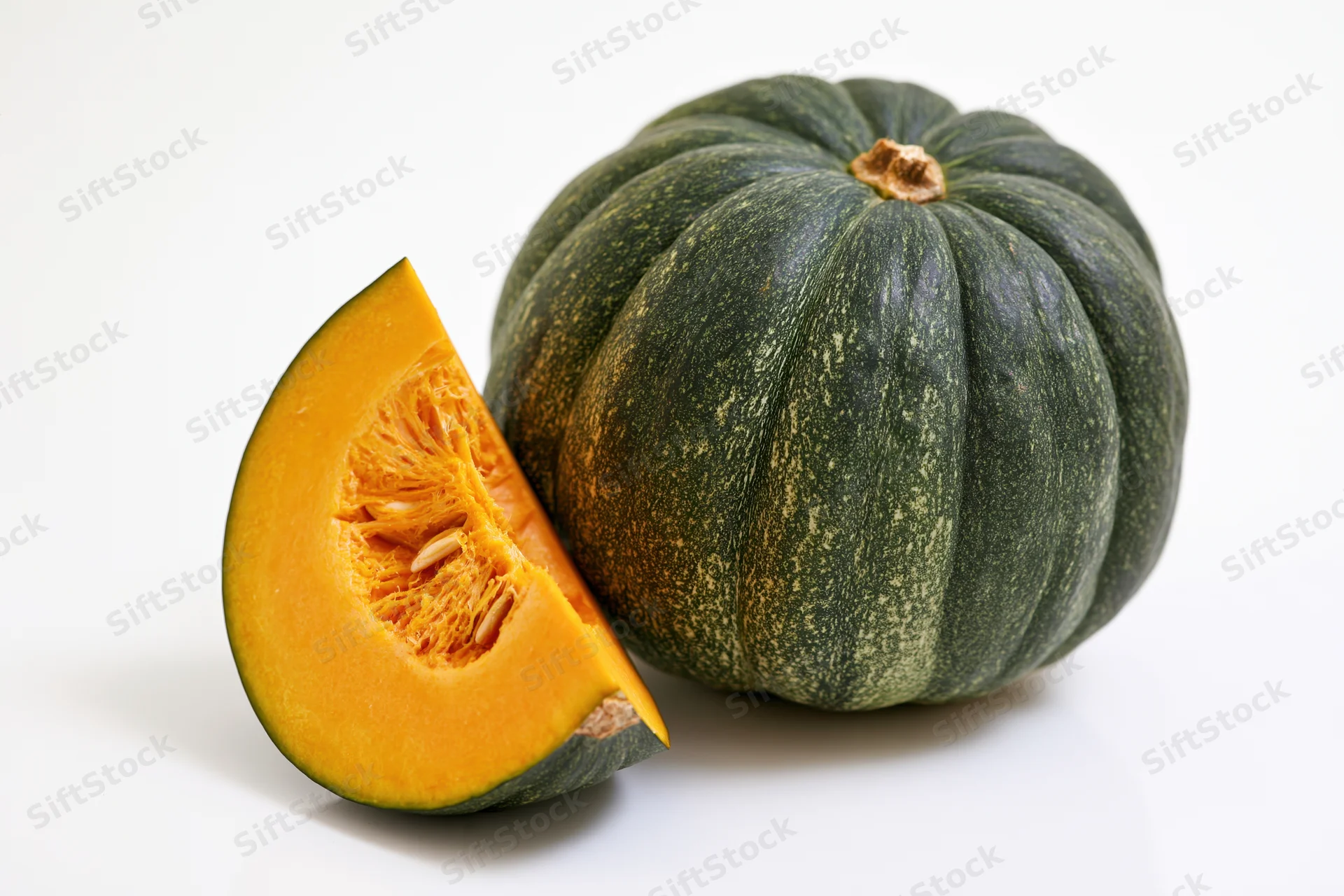 Whole kabocha squash with a cut slice beside it on a white background