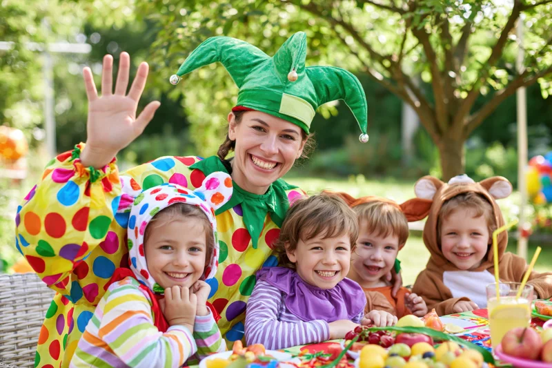 Woman in jester costume waving with children in costumes at outdoor party table