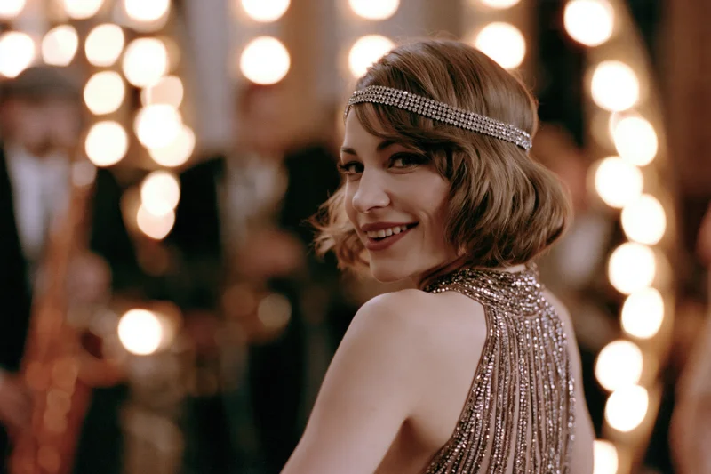 Young woman in 1920s beaded halter gown glancing back at camera at a jazz party