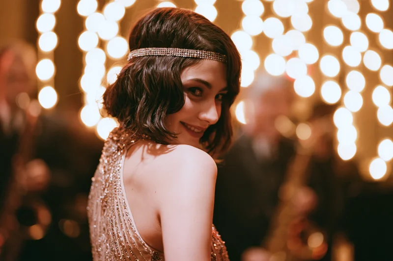 Young woman in 1920s-style beaded halter gown glancing back at camera at festive party with bokeh lights in background