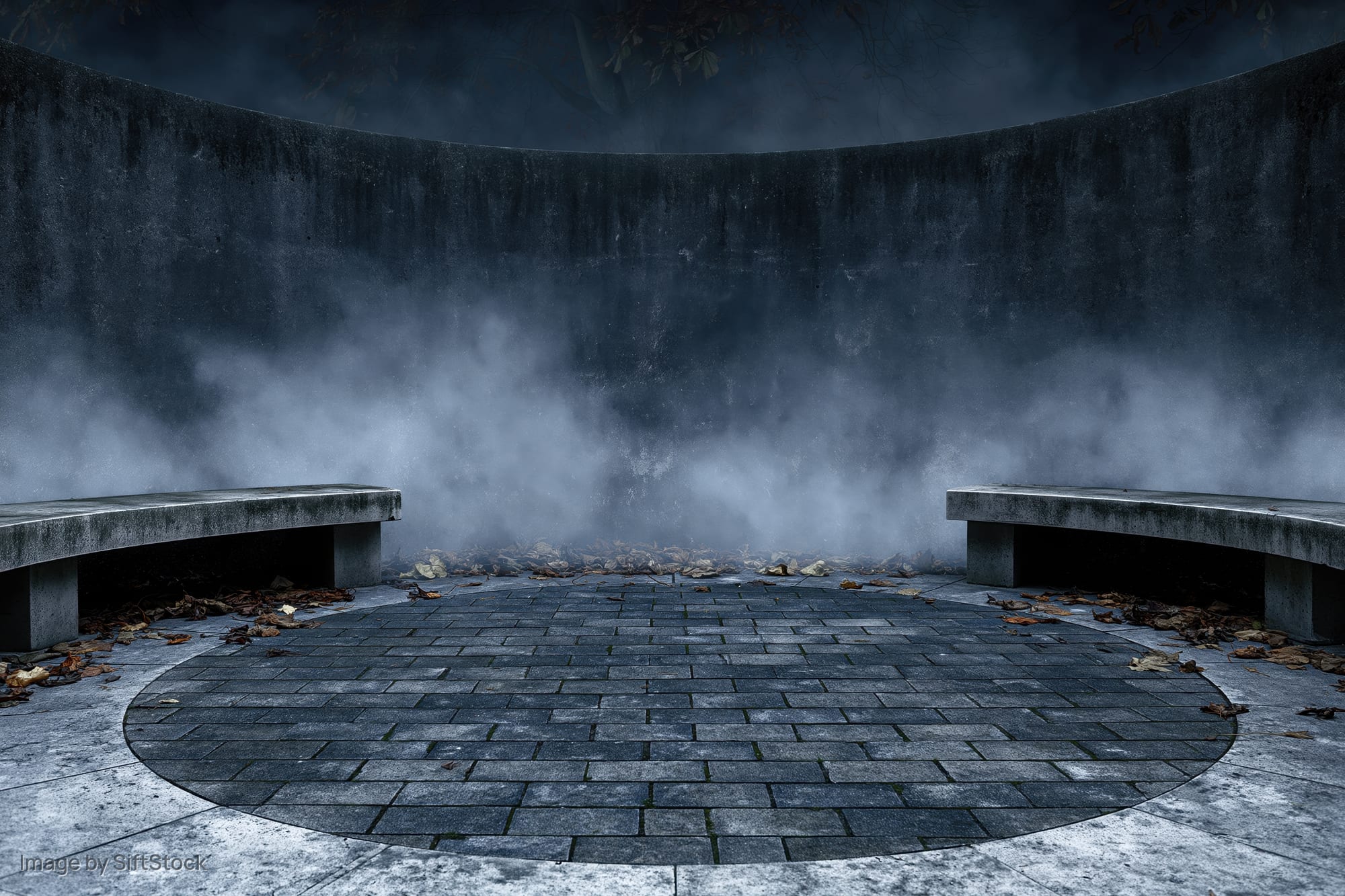 Circular stone courtyard at night with fog and two benches, surrounded by weathered walls and scattered leaves