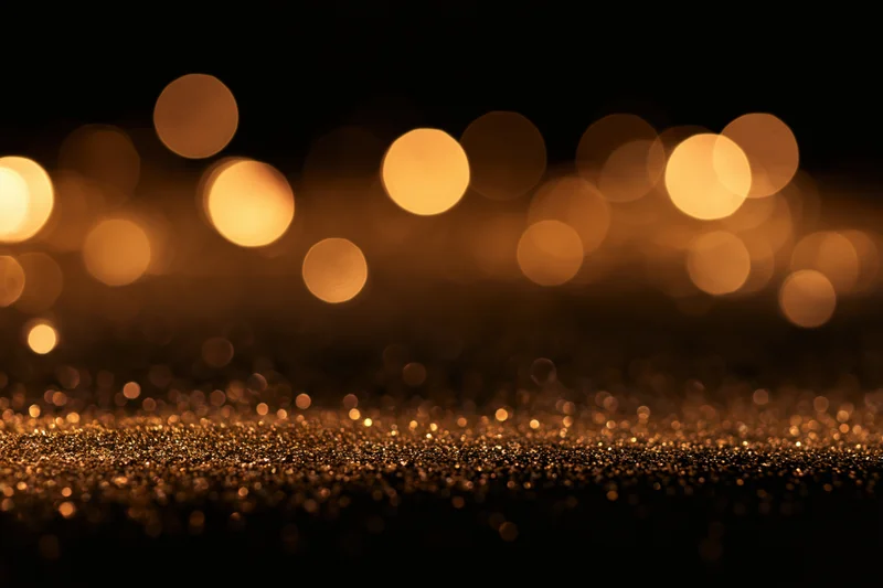 Abstract bokeh lights with glittering gold particles on dark background