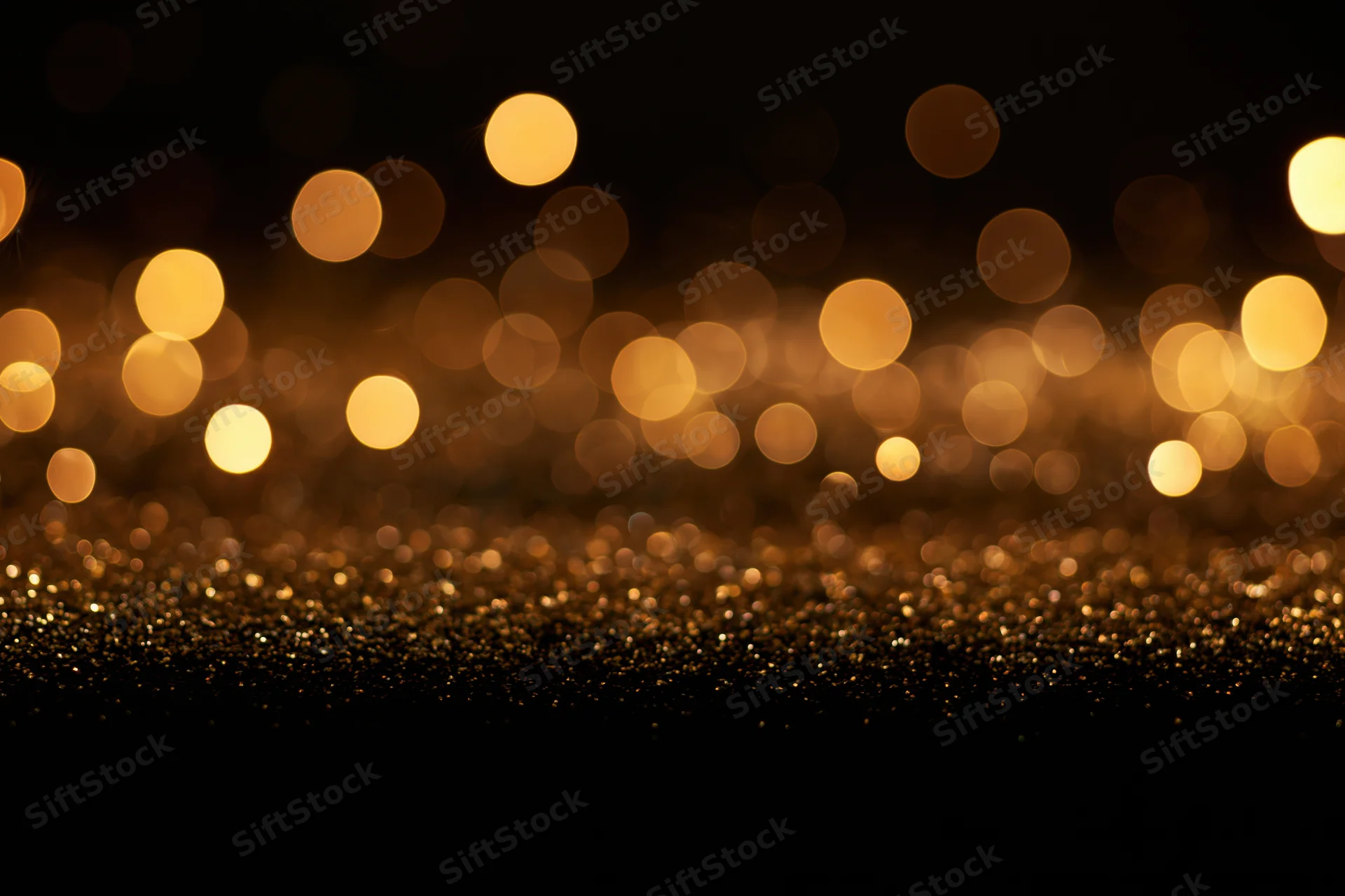 Abstract bokeh lights in warm gold and amber over glittering surface with copyspace below