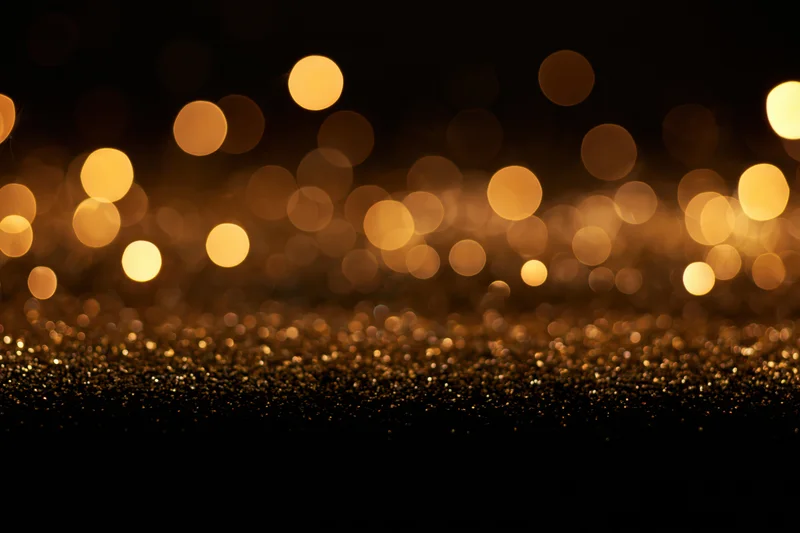 Abstract bokeh lights in warm gold and amber over glittering surface with copyspace below