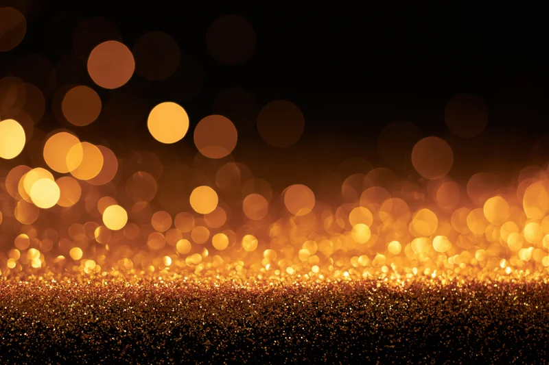 Abstract bokeh background with scattered warm gold and amber lights over glittering surface