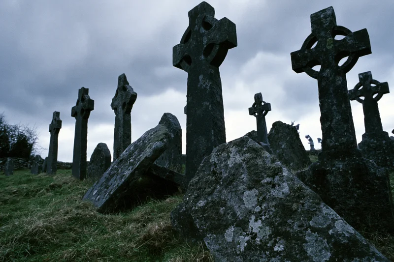 Weathered celtic cross headstones in an ancient irish graveyard under a cloudy sky