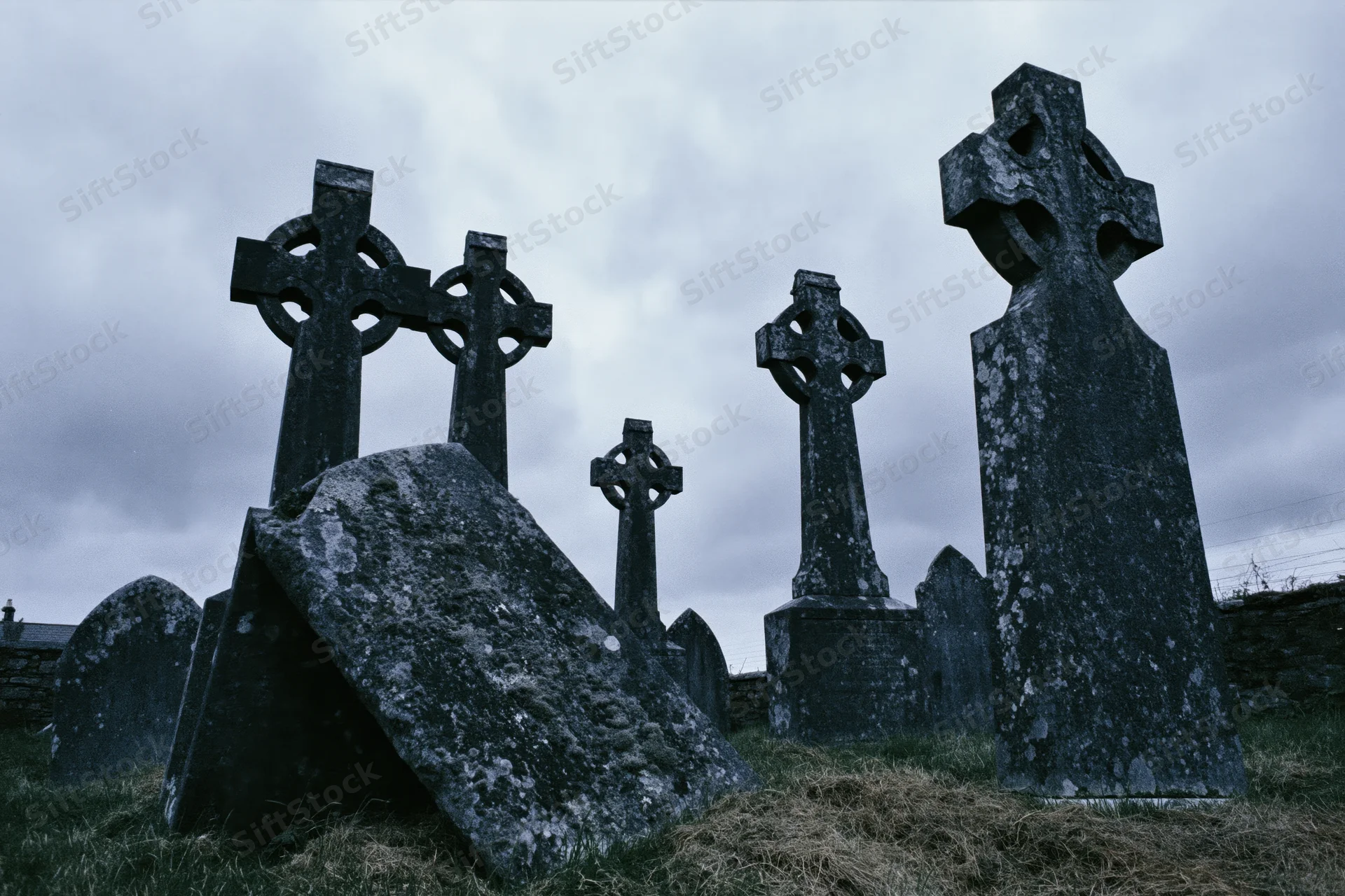Weathered celtic cross headstones in an ancient irish graveyard under a cloudy sky