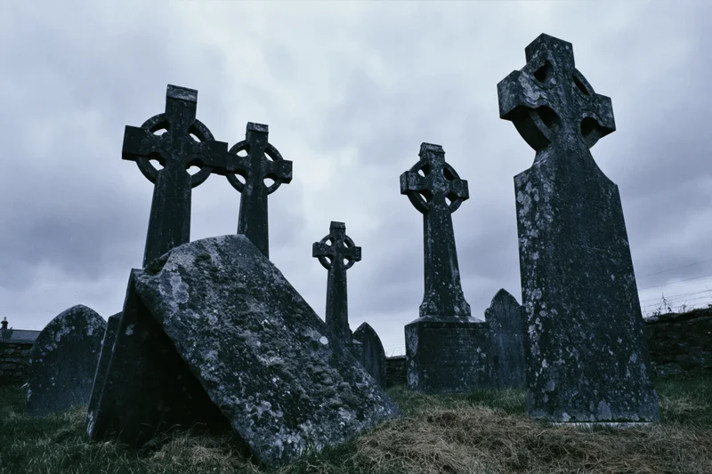 Weathered celtic cross headstones in an ancient irish graveyard under a cloudy sky