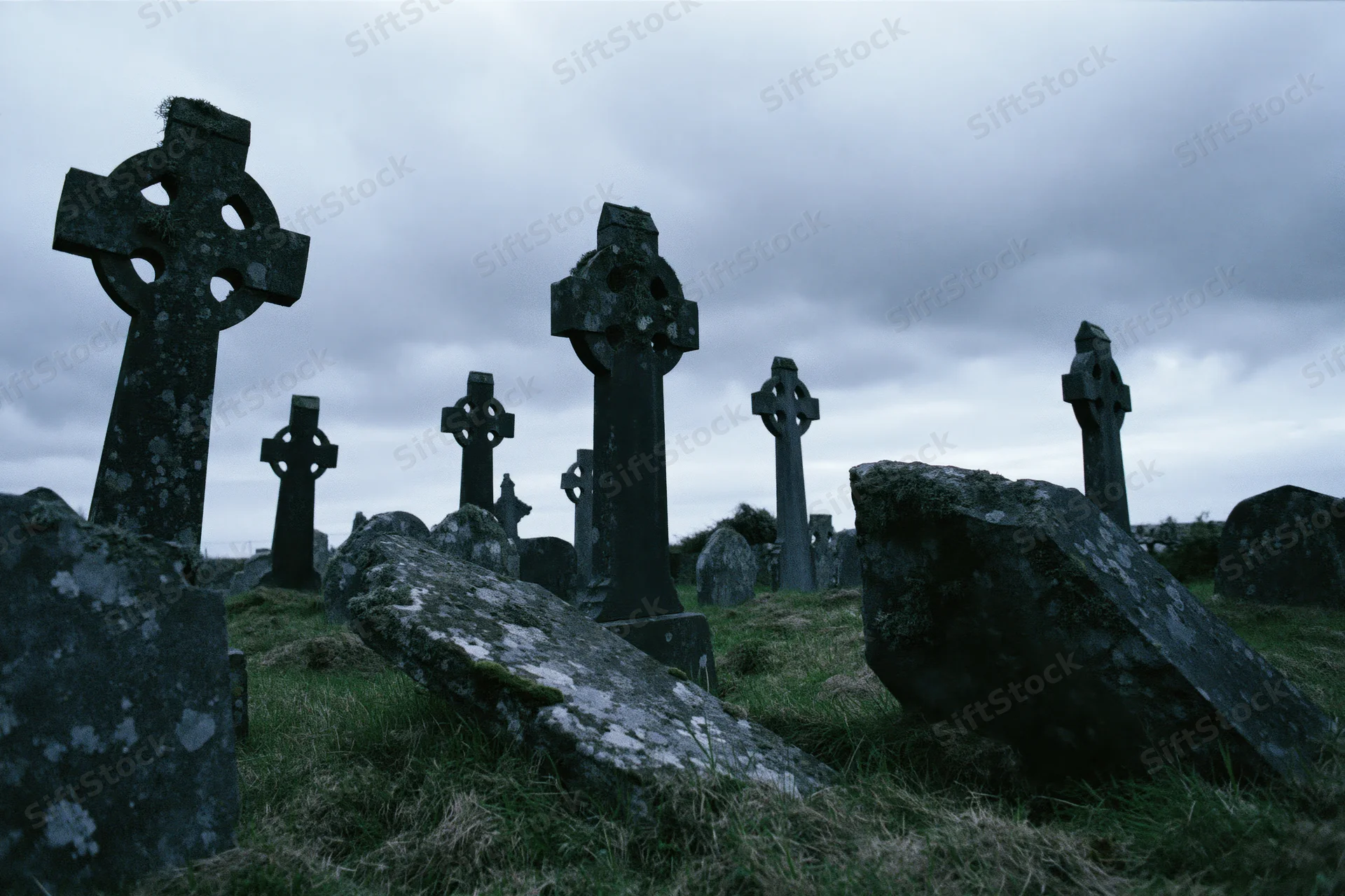 Weathered celtic cross headstones in an ancient irish graveyard under an overcast sky