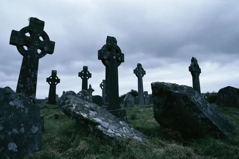 Weathered celtic cross headstones in an ancient irish graveyard under an overcast sky