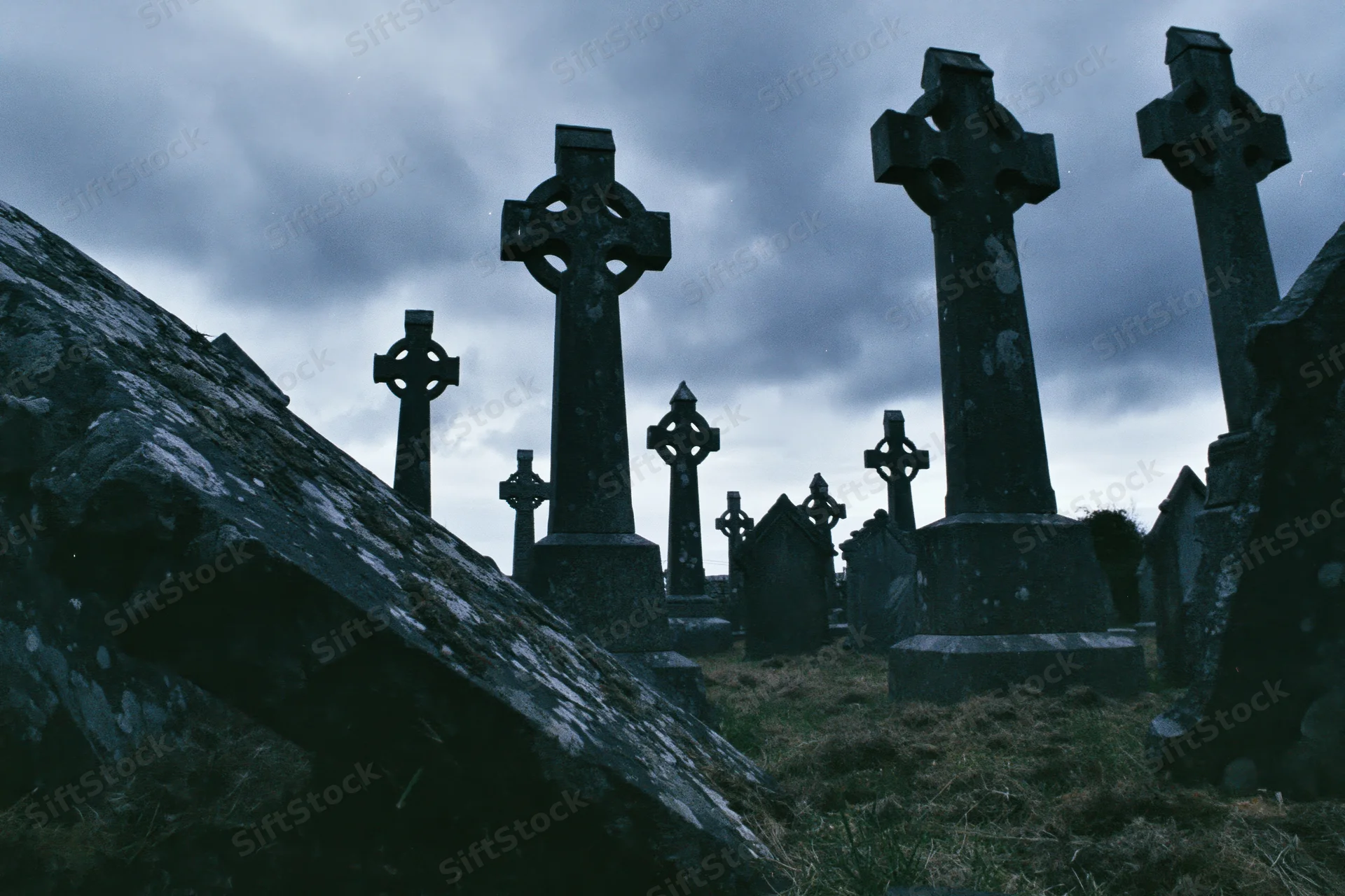 Weathered celtic cross headstones in an ancient irish graveyard under a cloudy sky