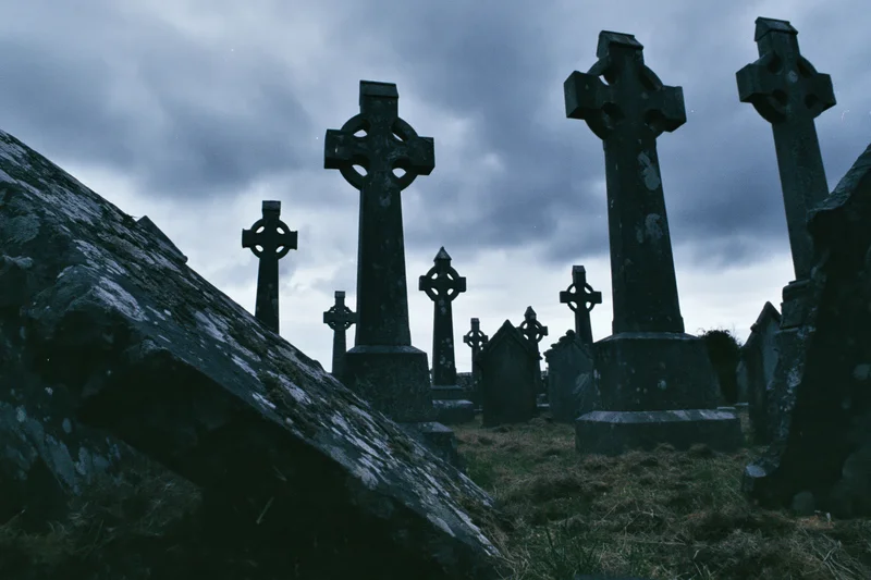 Weathered celtic cross headstones in an ancient irish graveyard under a cloudy sky