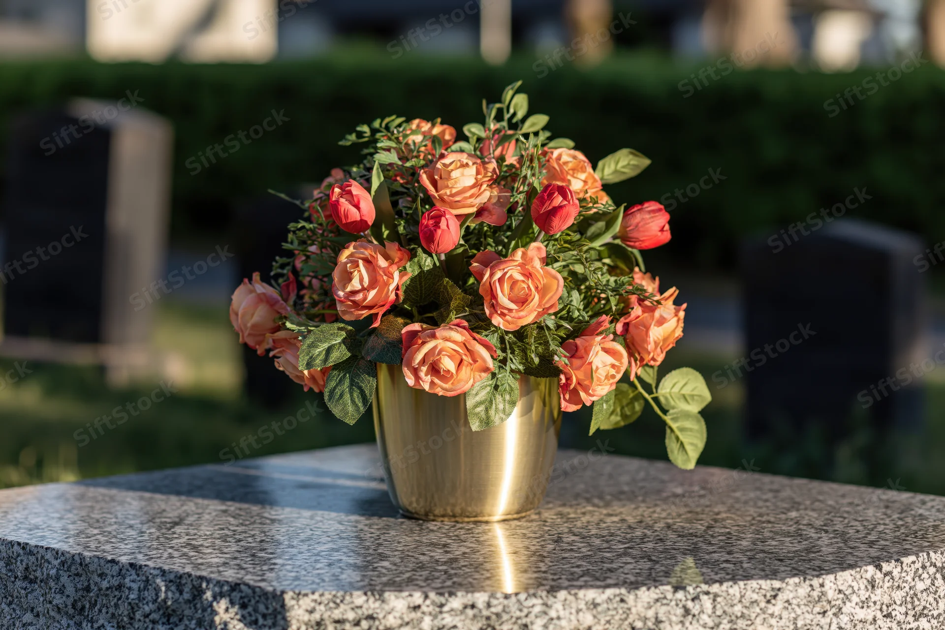 Artificial roses in a gold vase on a granite tombstone in a cemetery