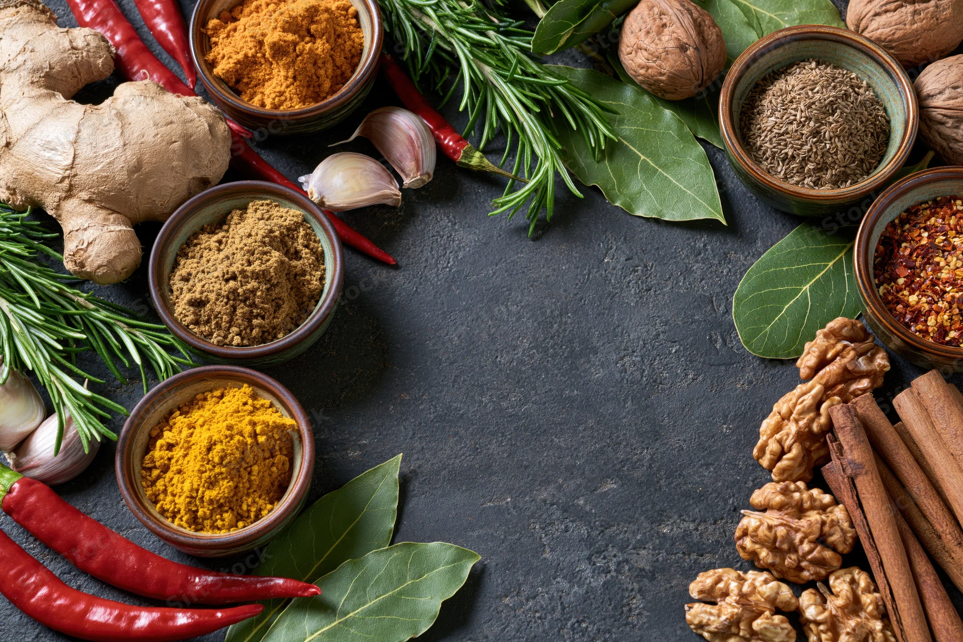 Assorted spices and herbs arranged in a flat lay on a dark stone surface with copyspace