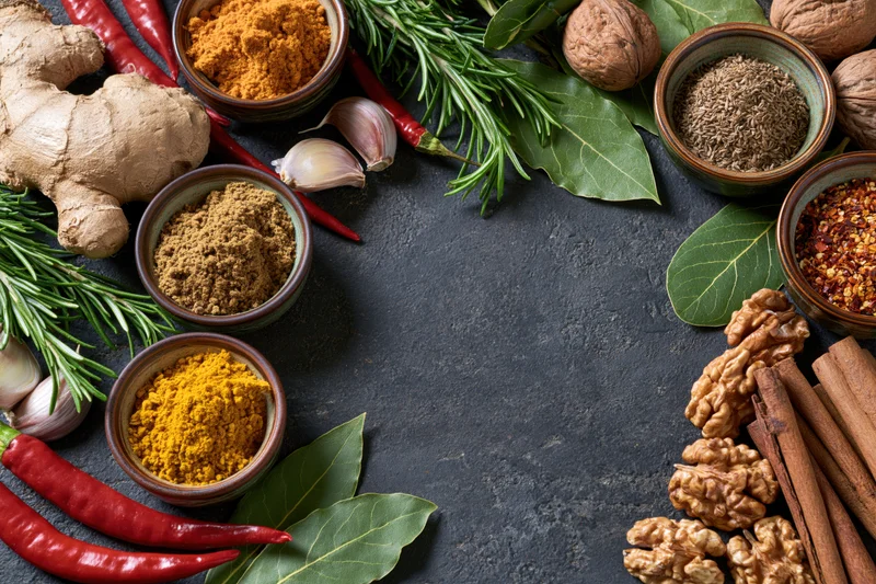Assorted spices and herbs arranged in a flat lay on a dark stone surface with copyspace