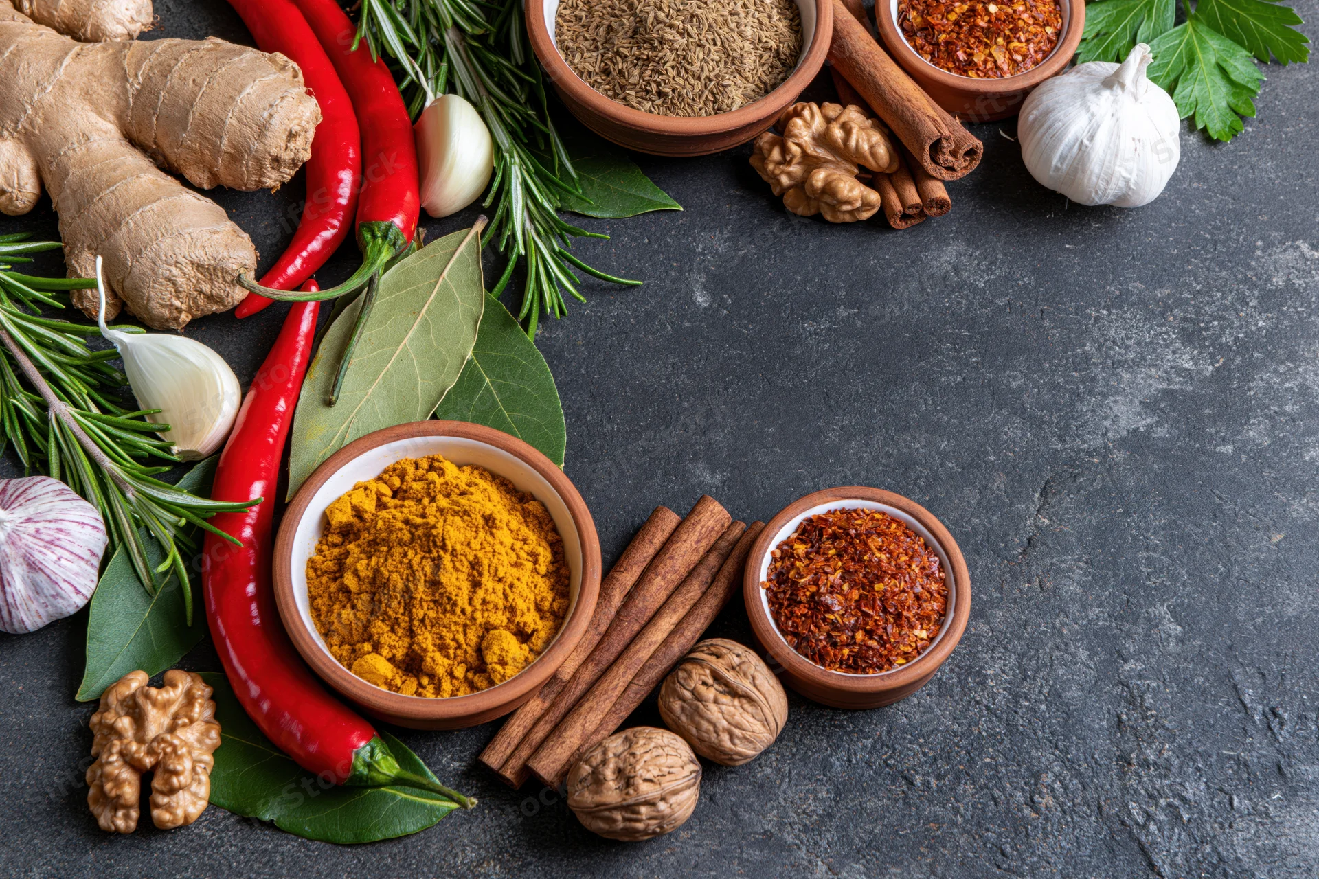 Assorted spices and herbs arranged in a flat lay on dark stone surface with copyspace
