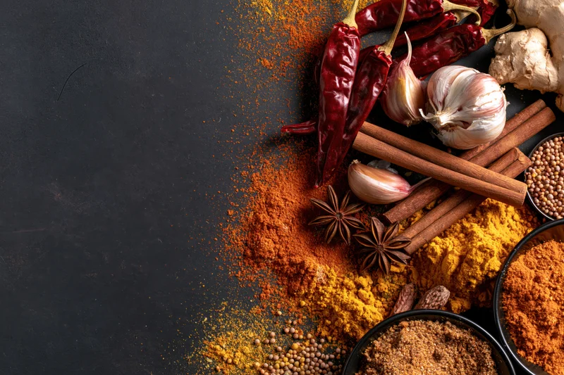 Assorted whole and ground spices arranged along the right side of a dark surface with copyspace on the left