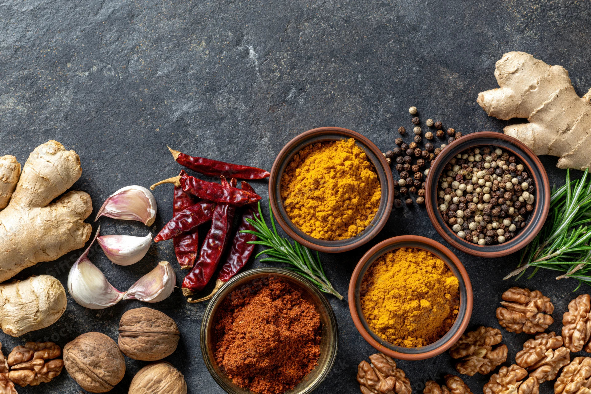 Assorted whole and ground spices arranged on dark stone surface with copyspace
