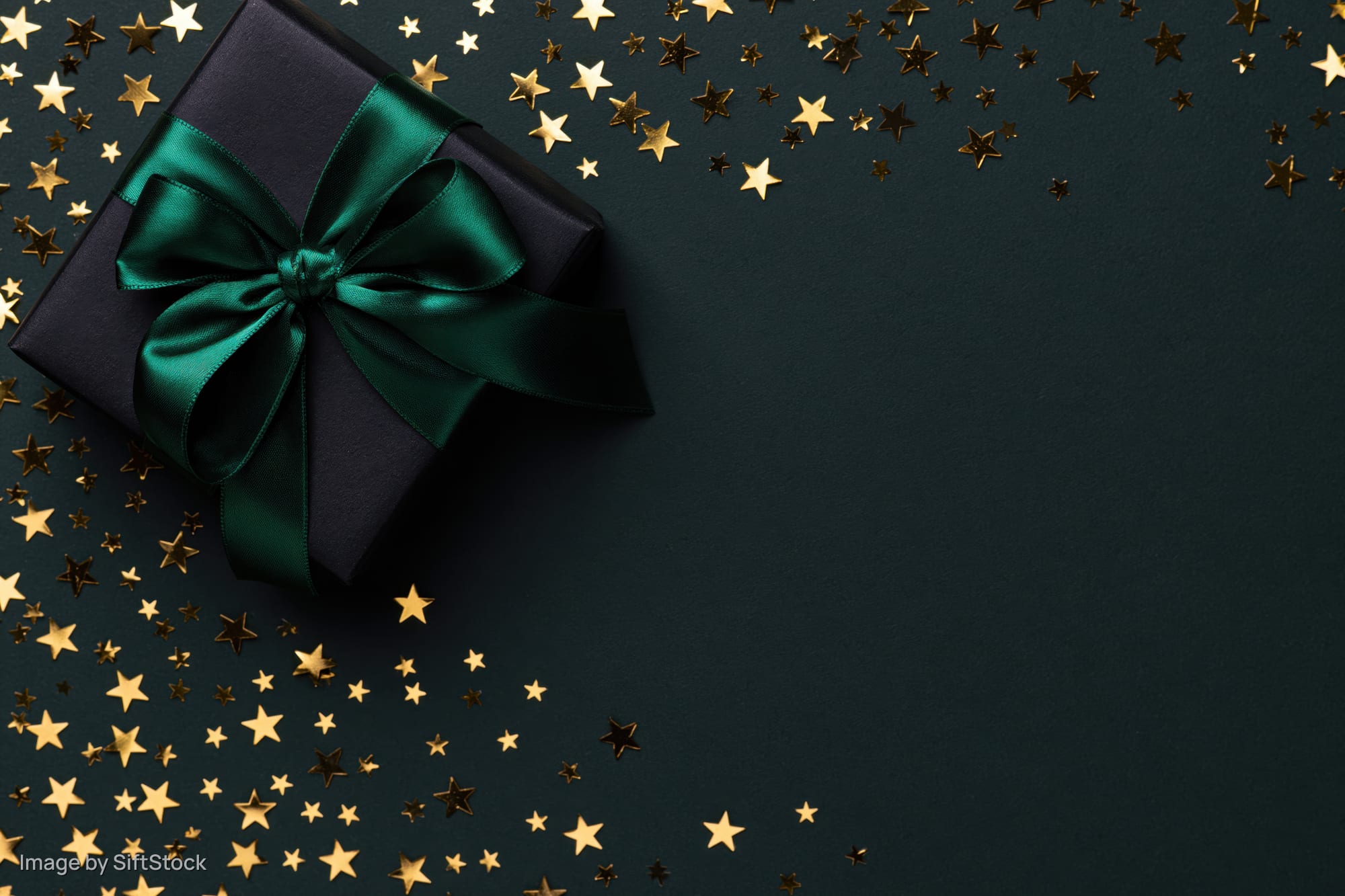Black gift box with emerald green satin ribbon and gold star confetti on dark surface