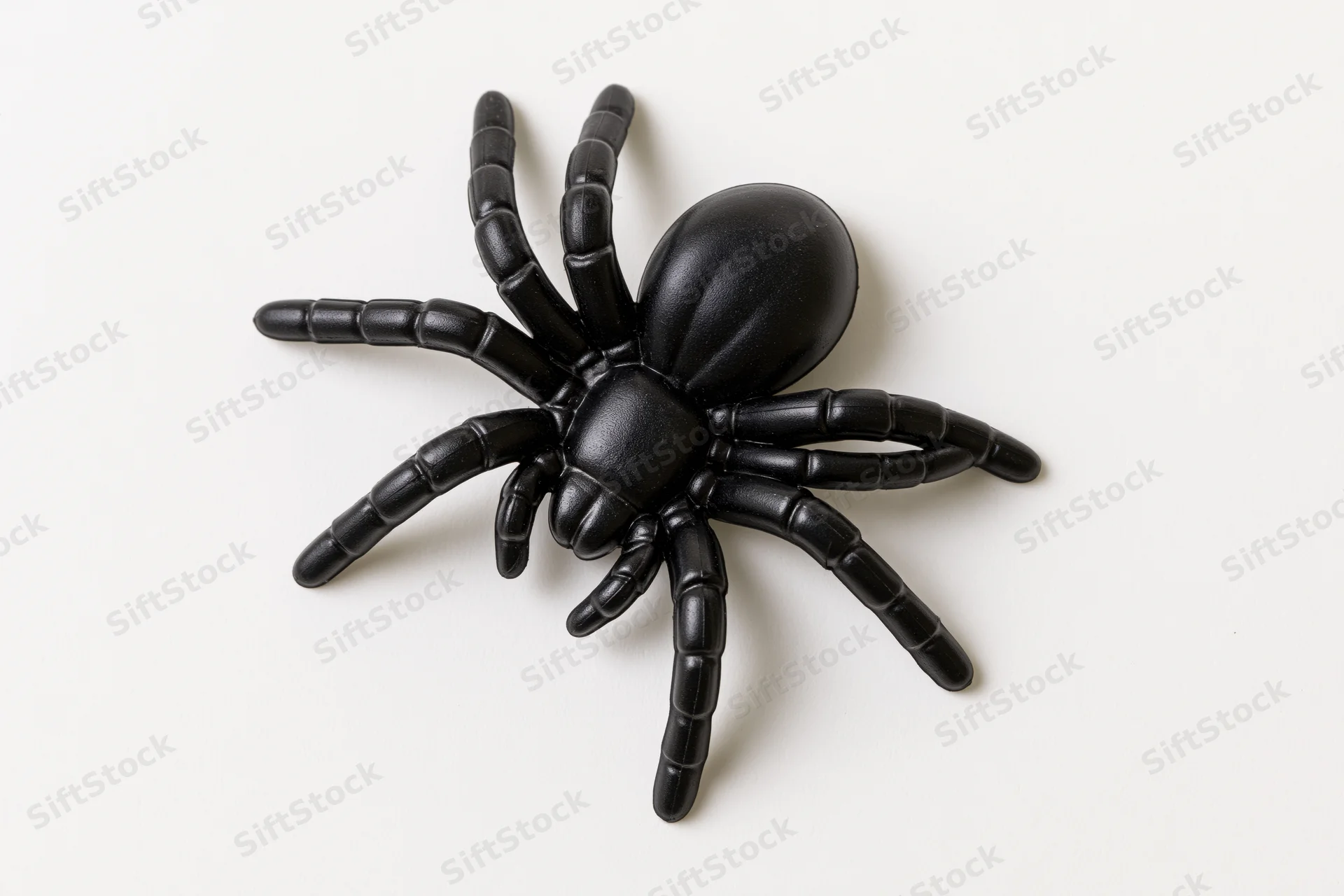 Black plastic toy spider lying flat on a white surface