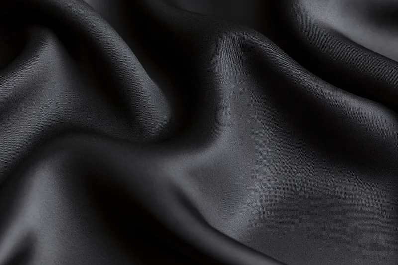 Closeup of black silk fabric draped in soft folds filling the frame