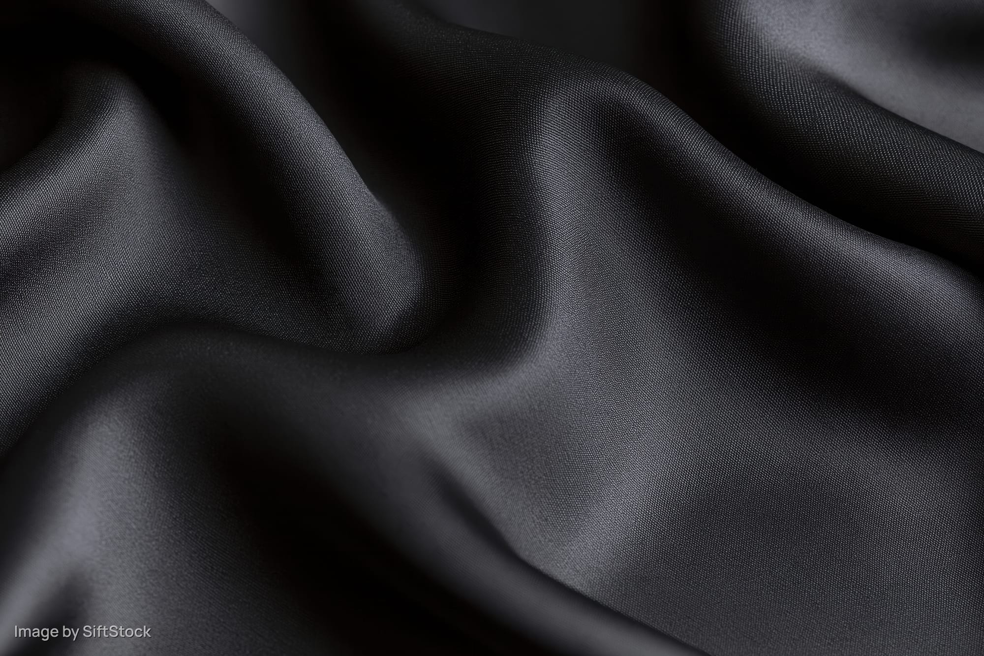 Closeup of black silk fabric draped in soft folds filling the frame