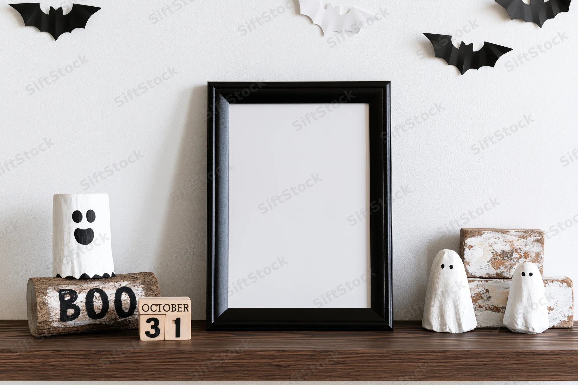 Blank black frame on wooden shelf with halloween decorations including ghosts, bats, and a boo log