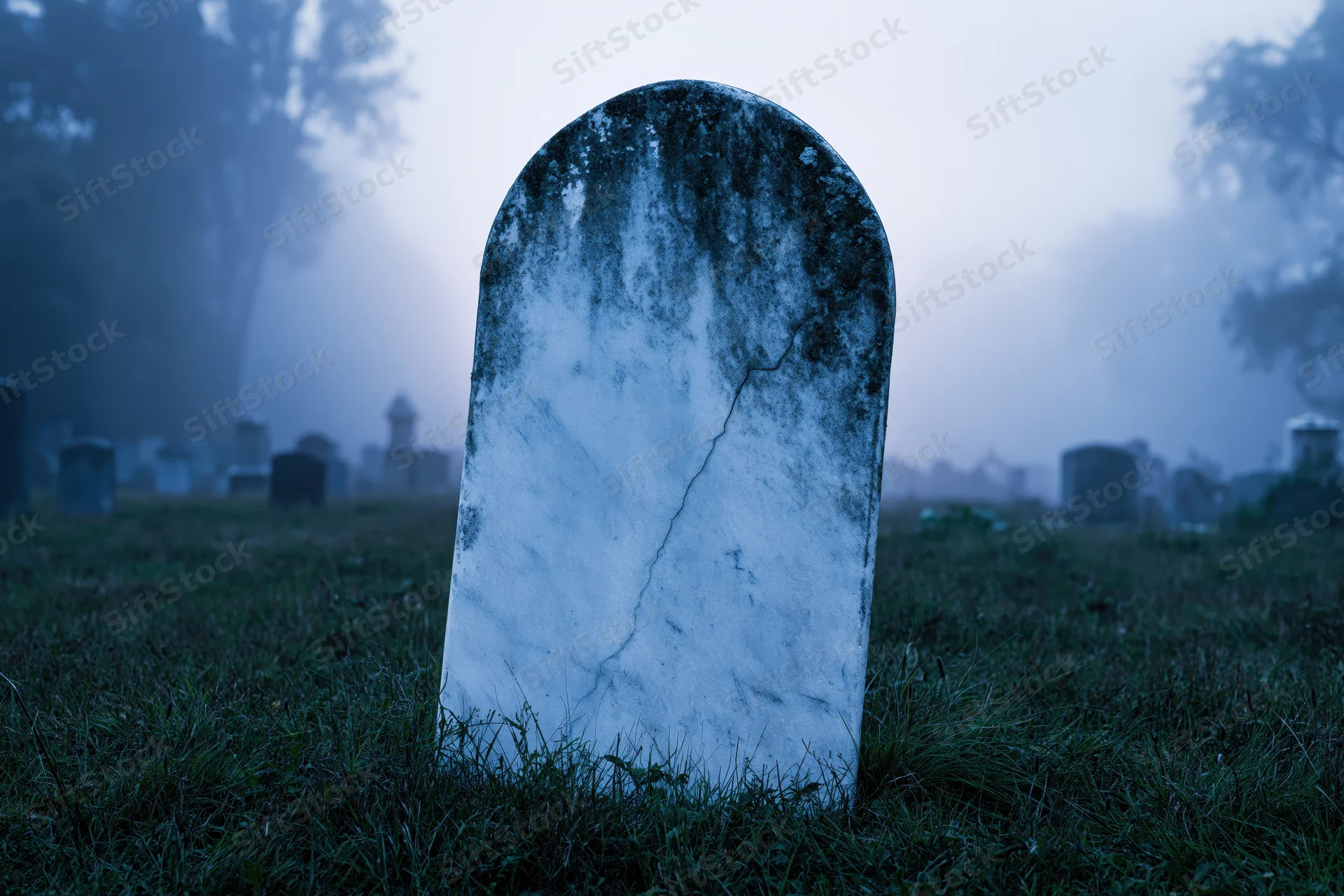 Weathered marble gravestone standing upright in foggy cemetery at dawn