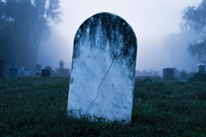 Weathered marble gravestone standing upright in foggy cemetery at dawn