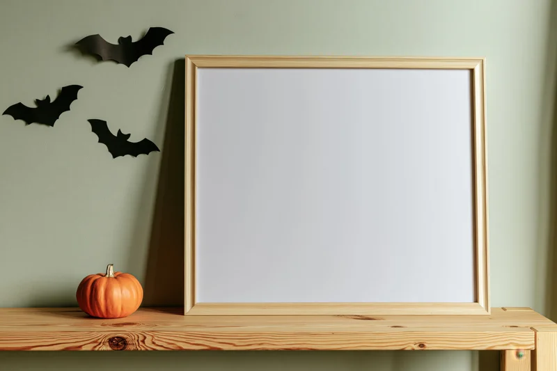 Blank white picture frame with thin light wood border on wooden shelf beside halloween decorations
