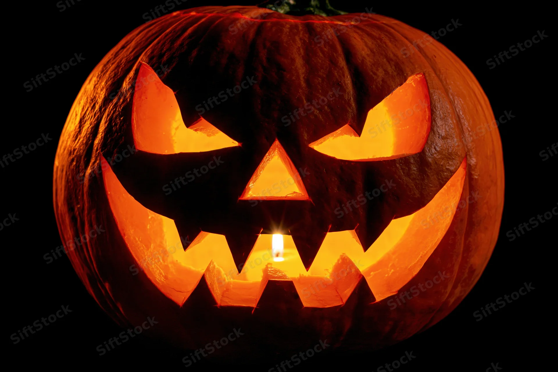 Carved pumpkin with glowing face lit by candle against black background