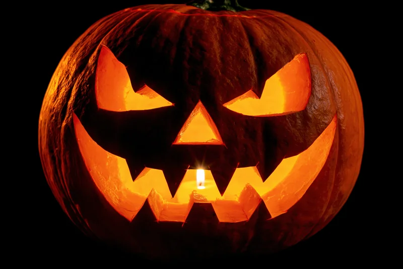 Carved pumpkin with glowing face lit by candle against black background