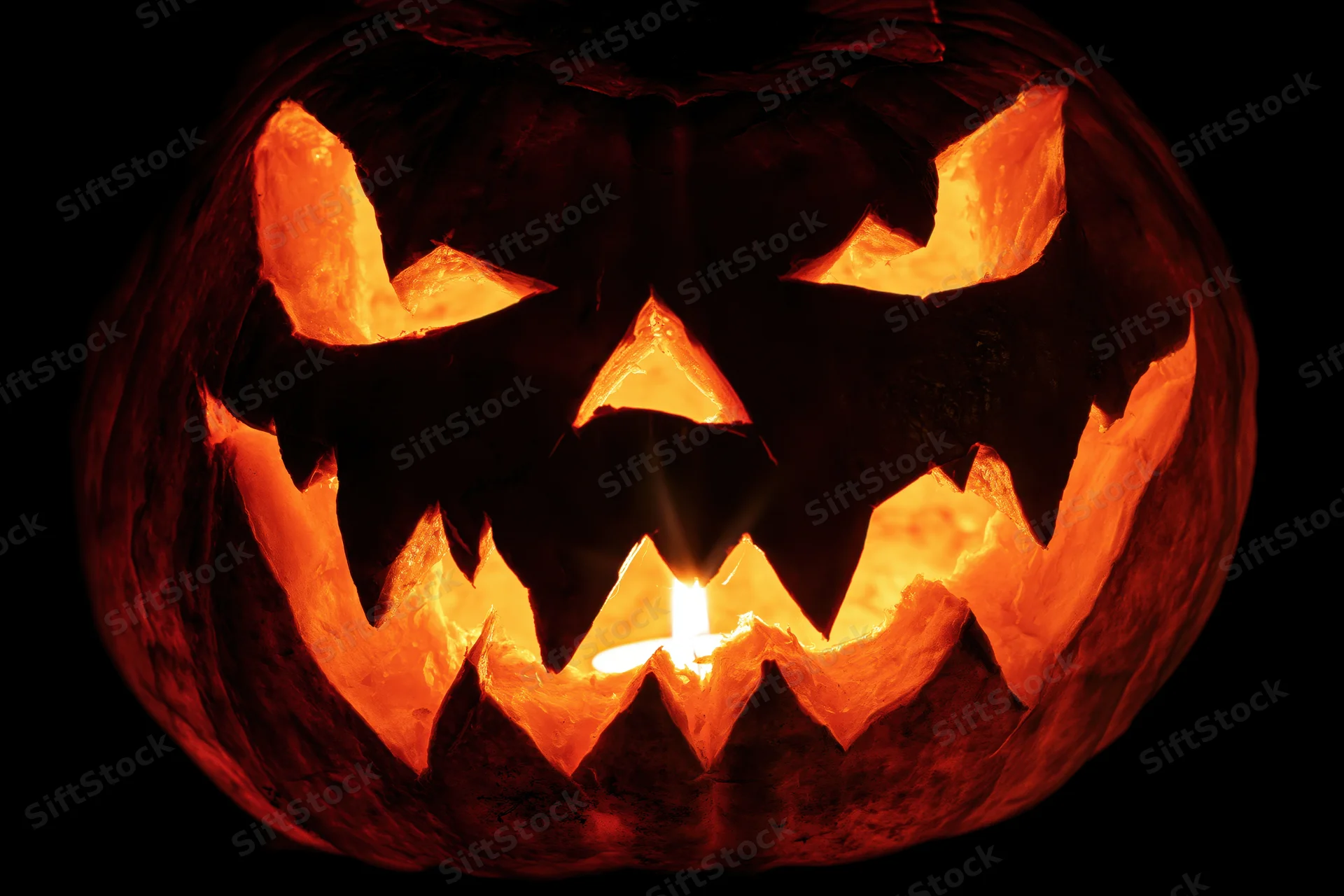 Carved pumpkin with glowing candle inside against black background