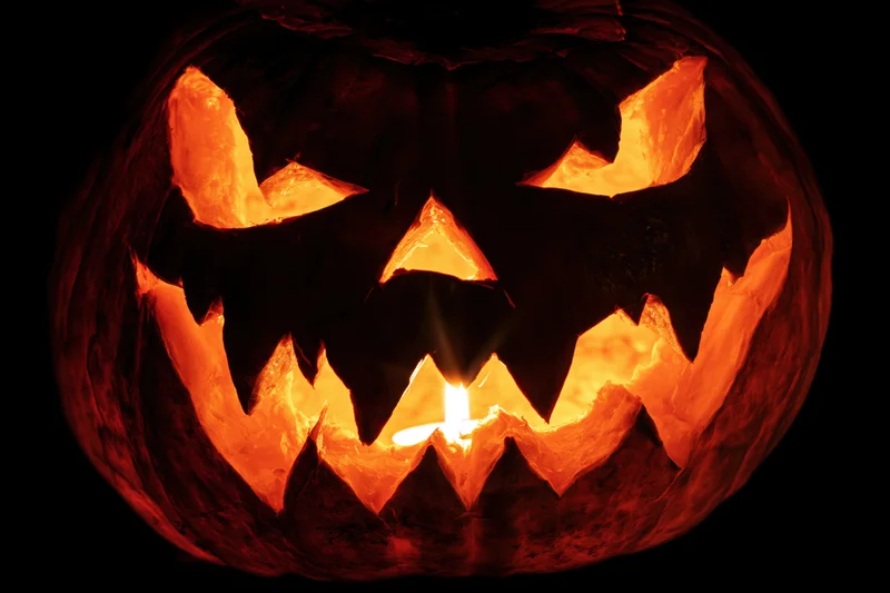 Carved pumpkin with glowing candle inside against black background