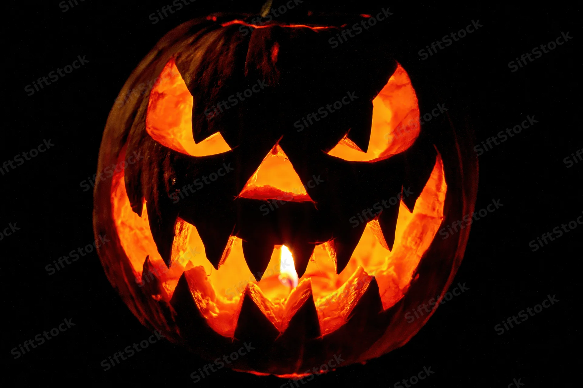 Carved pumpkin with glowing face lit by candle against black background
