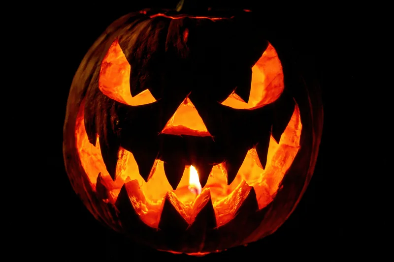 Carved pumpkin with glowing face lit by candle against black background