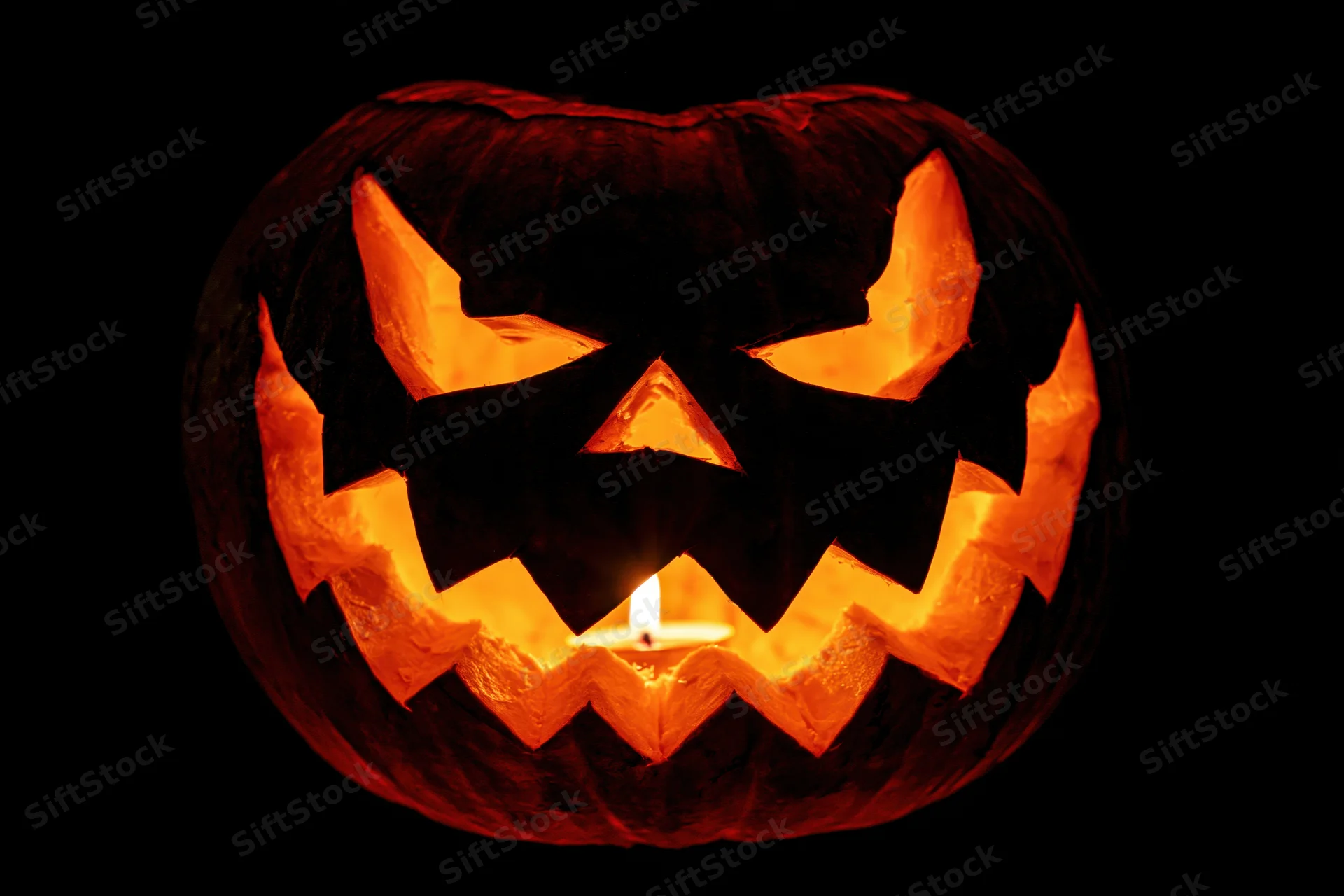 Carved pumpkin with glowing candle inside against black background