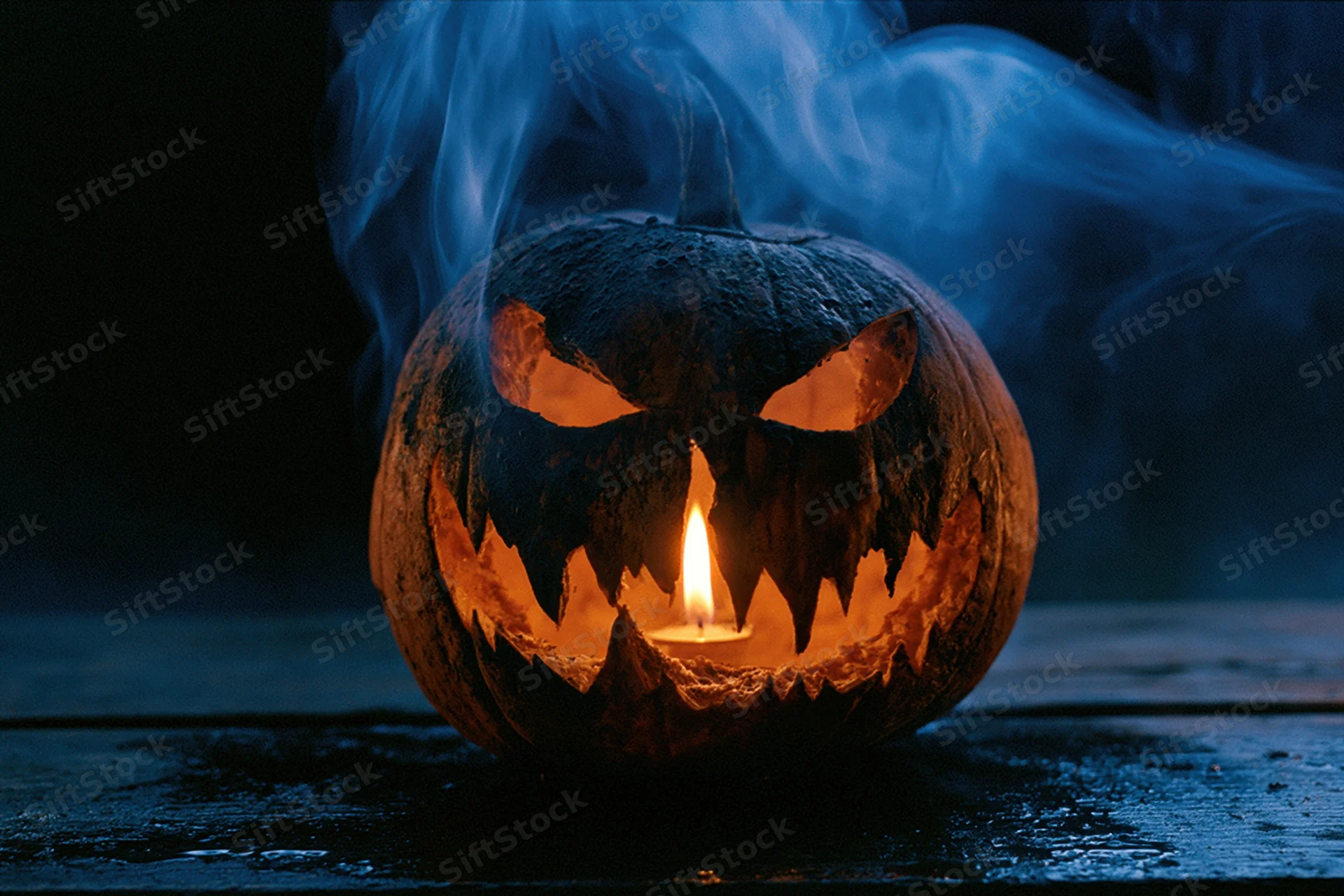 Carved jack-o-lantern glowing with candlelight and blue smoke on dark wooden surface
